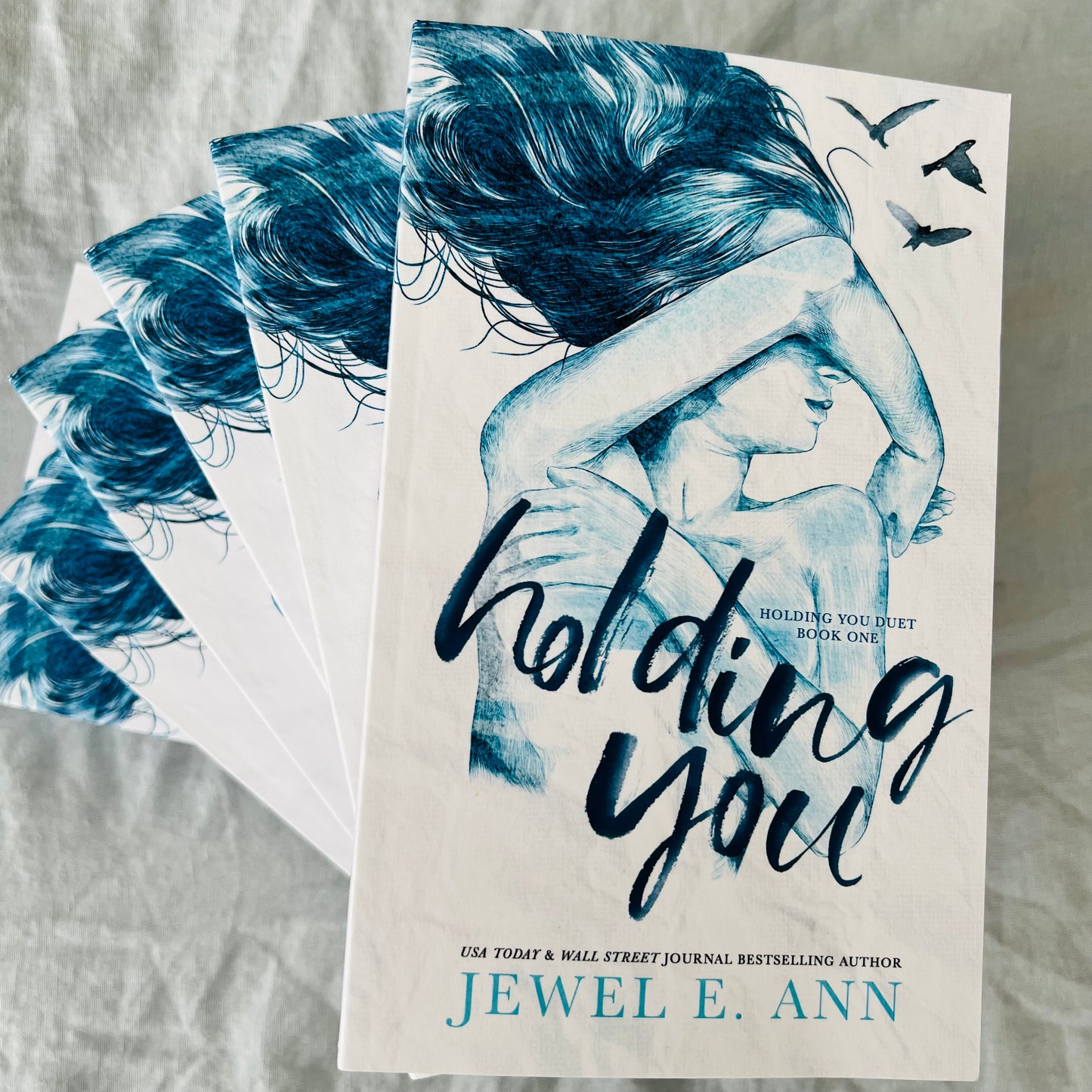 photo showing a stack of Holding You paperbacks by Jewel E. Ann on a white sheet